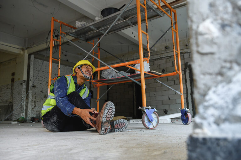 Construction worker sitting on the floor with ankle pain.