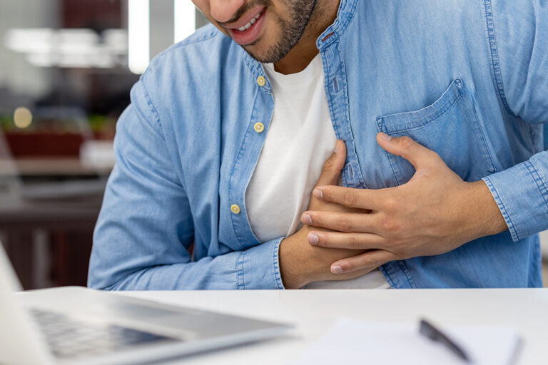 A man in a blue shirt clutches his chest with both hands and appears to be in pain.