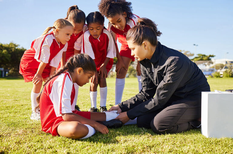 Young soccer players huddle around an injured teammate as their coach takes a look.