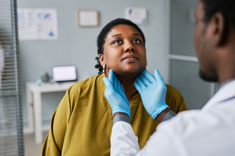 Doctor feeling womans throat in medical office